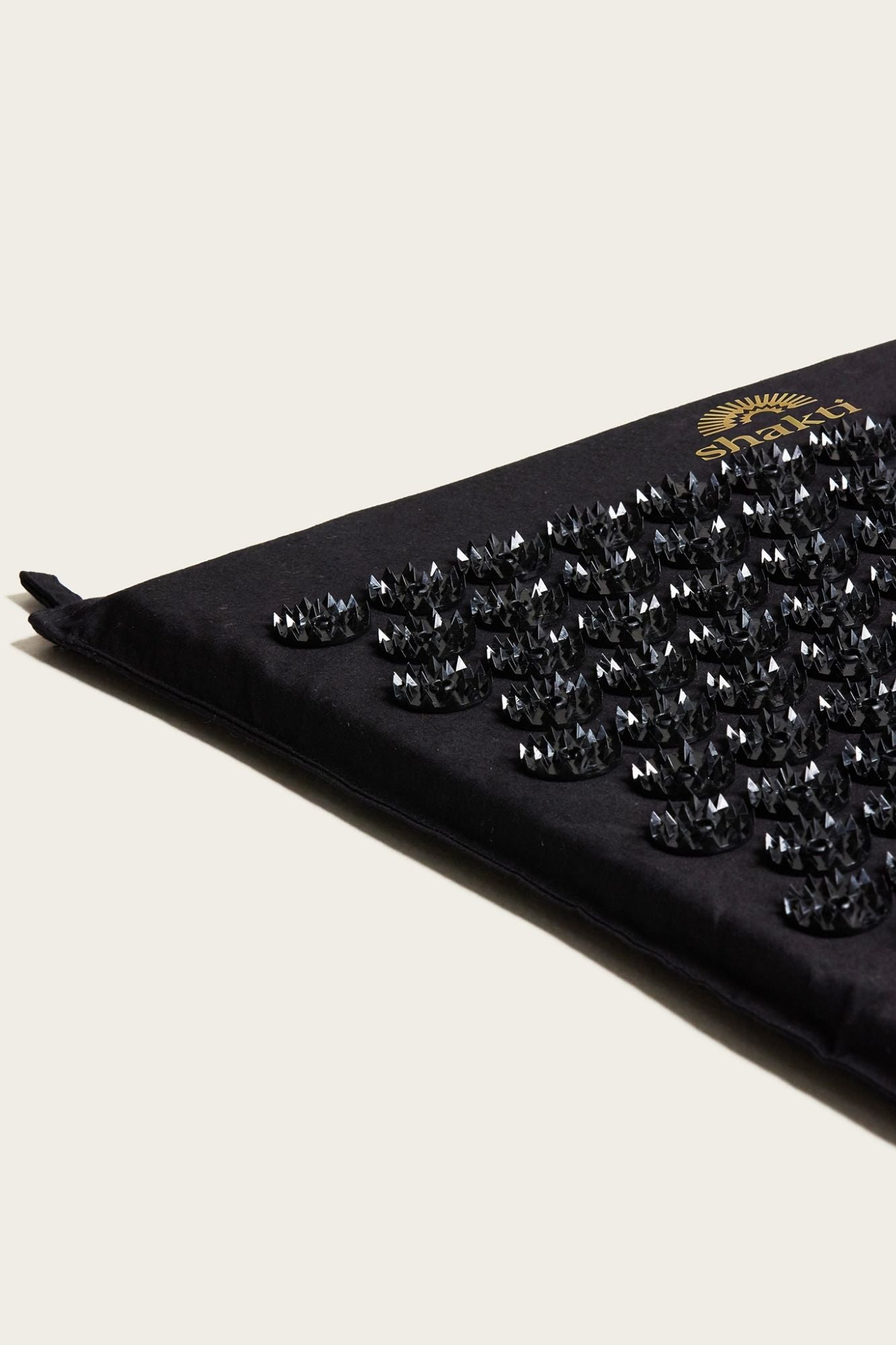 Close up of a Shakti Classic Acupressure Mat showing seams and hanging tabs on a light background.