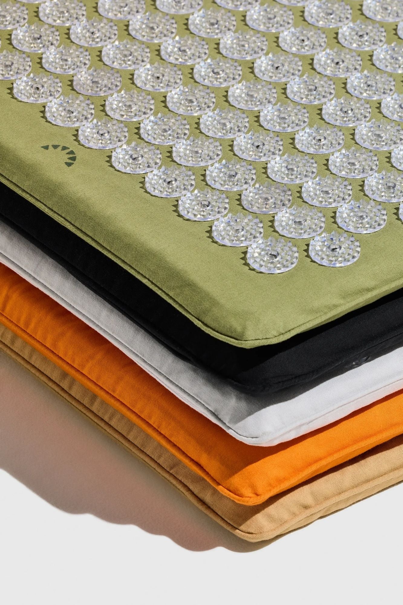 Close up of a stack of Shakti Premium Acupressure Mats showing rounded corners, piped seams and a range of neutral colours.