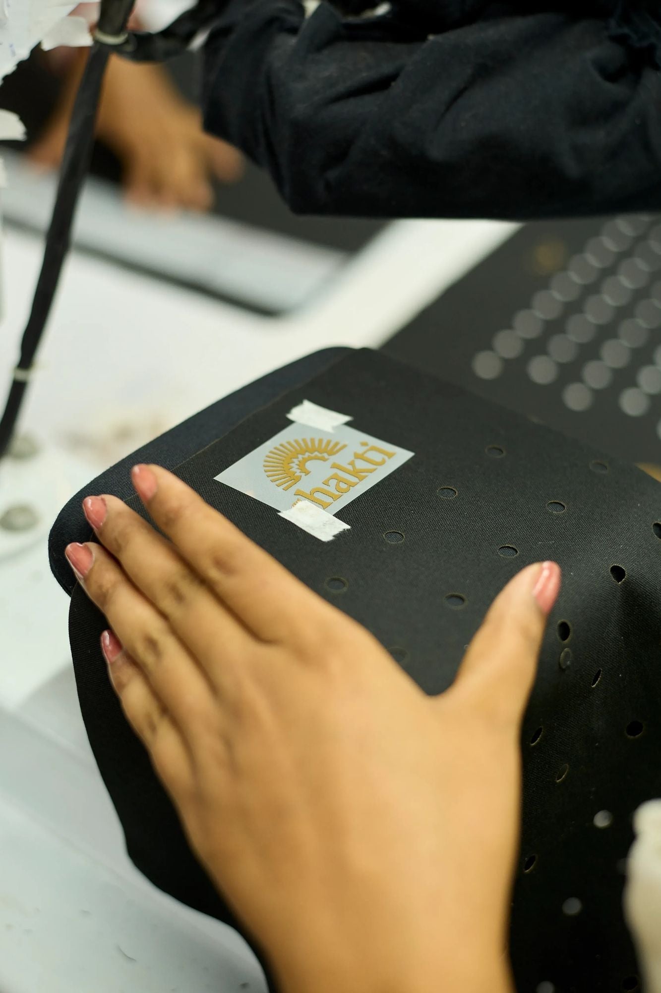 Close up of a persons hands preparing to screenprint the Shakti logo in Gold onto a Premium Acupressure Mat cover in Black.