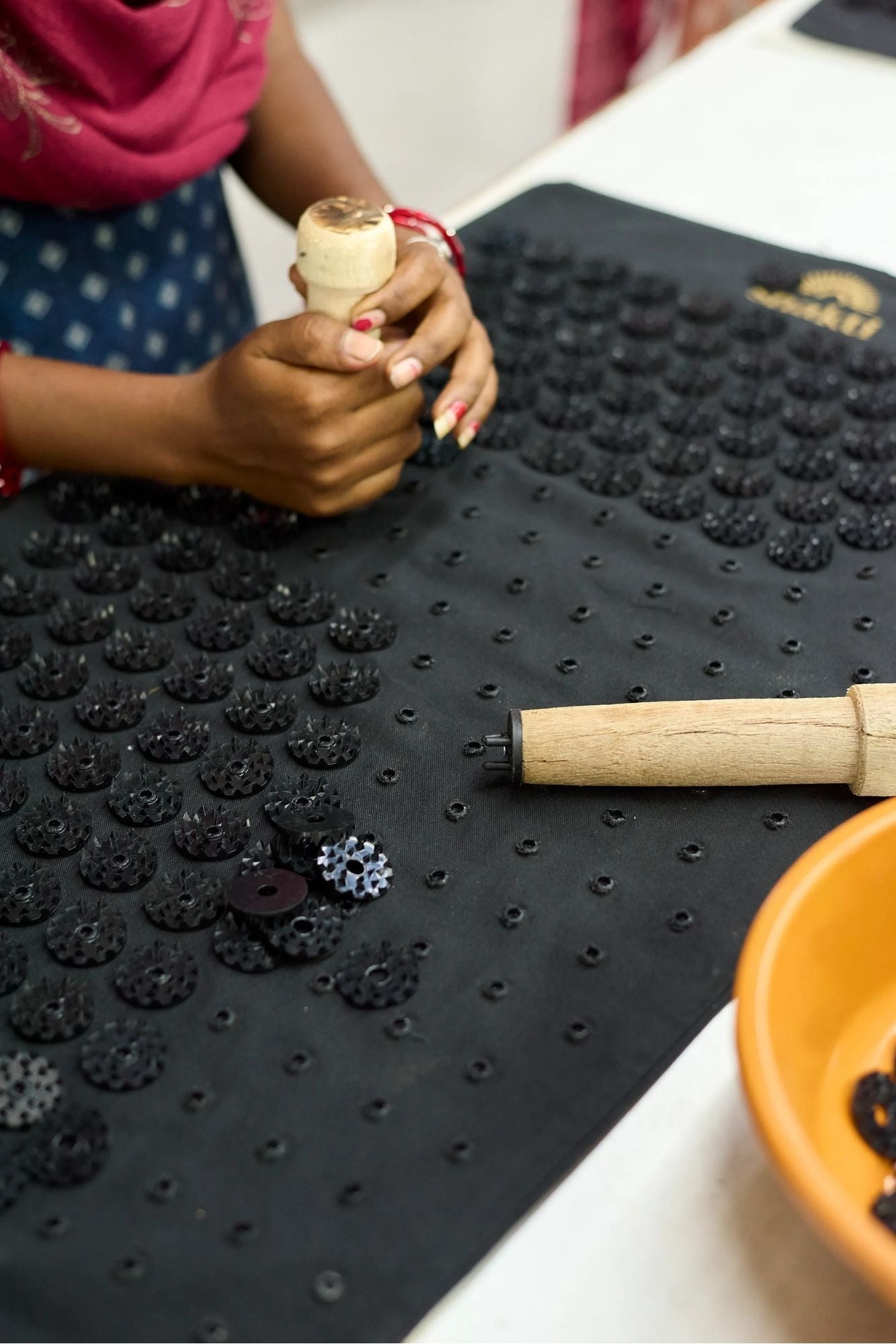Person hand-clipping signature Shakti spikes to a Premium Acupressure Mat in Black on with wooden tools on a table.