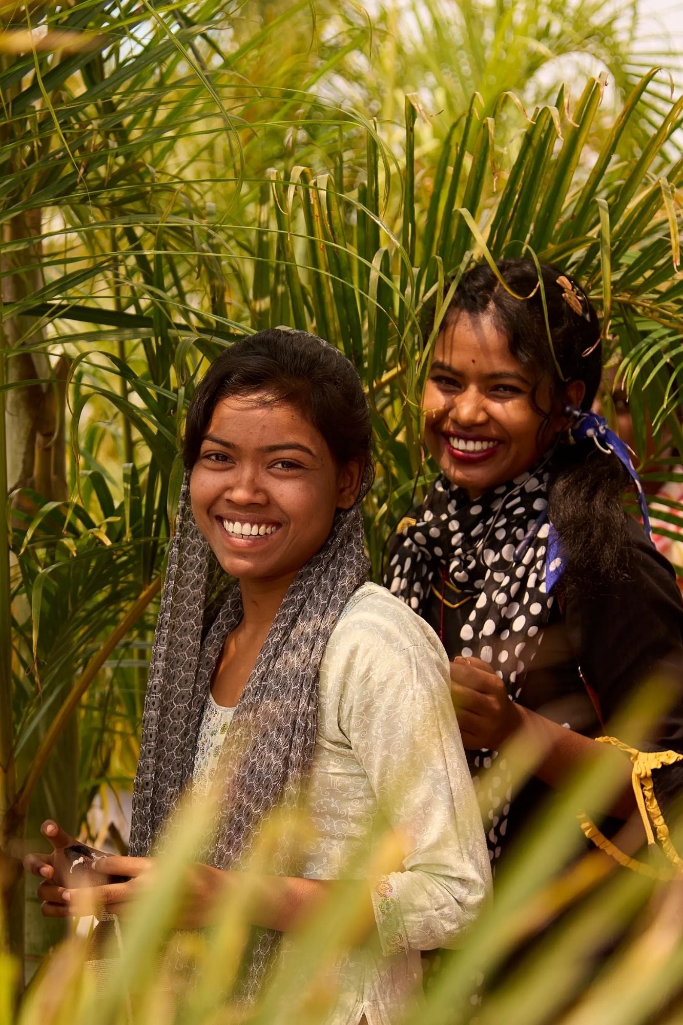 Two Indian women smiling in front of green foliage.