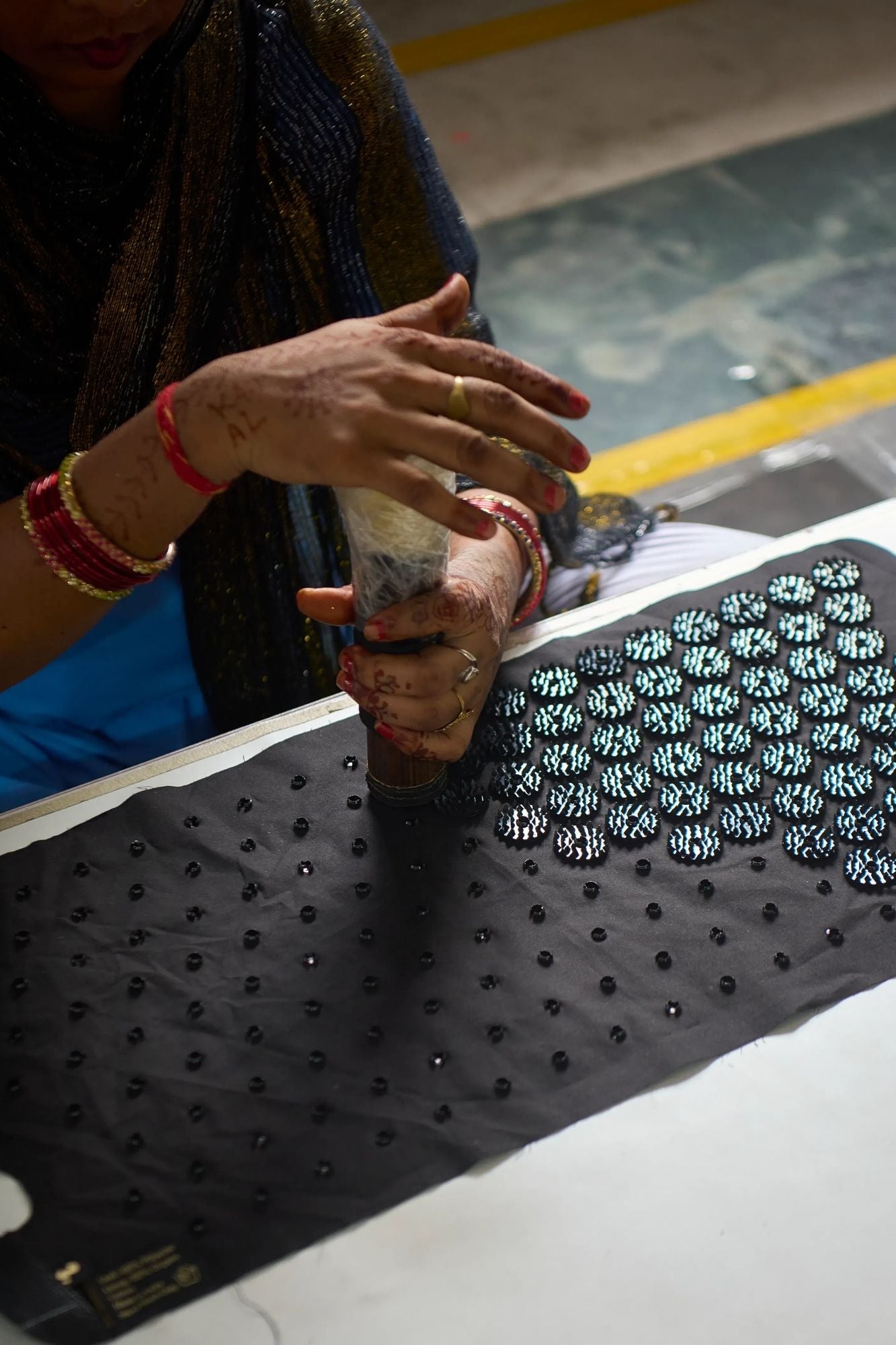 A close-up of a person hand clipping Shakti spikes on a Shakti Leg Wrap, wearing a dark patterned shawl and red bangles.